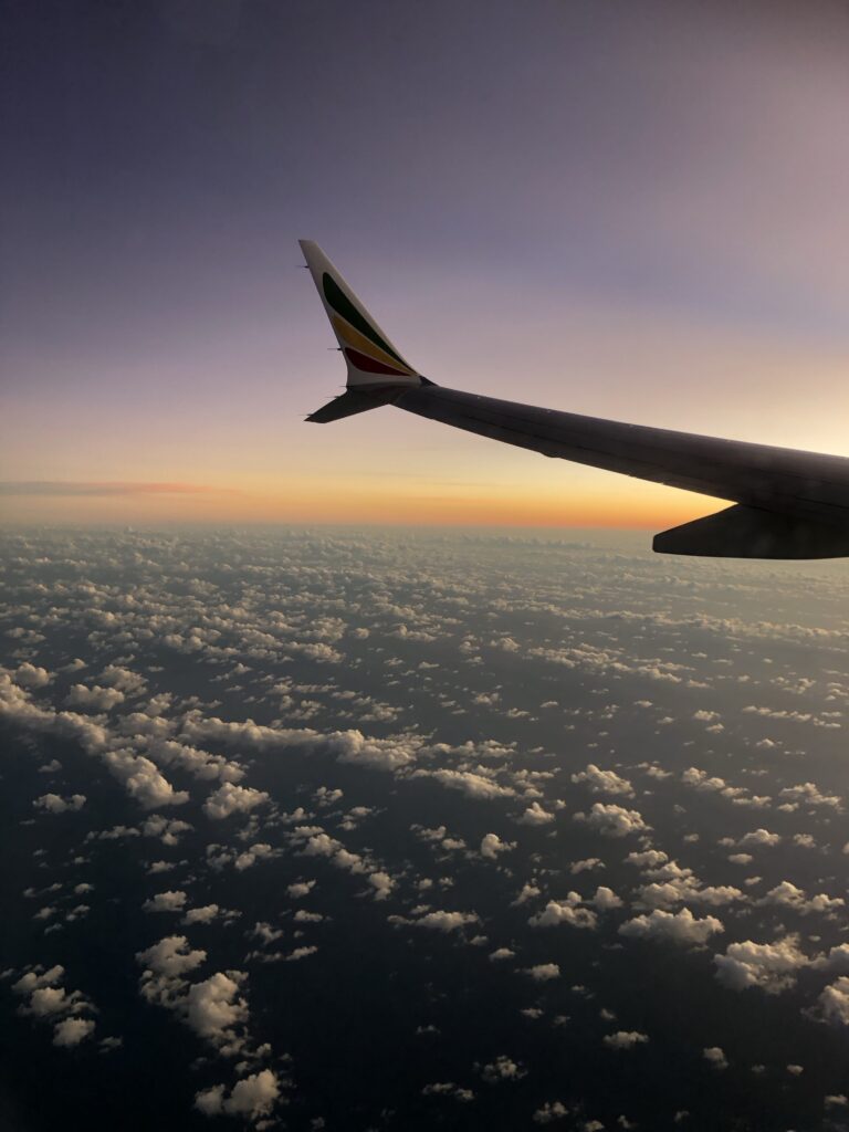 Die Tragfläche eines Flugzeugs über den Wolken mit Sonnenuntergang im Hintergrund. 