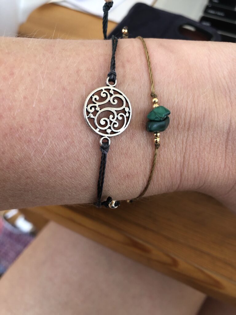 Zwei Armbänder. Eines mit zwei grünen Steinen und ein zweites, was ein silberner Kreis mit Ornamenten ist. 