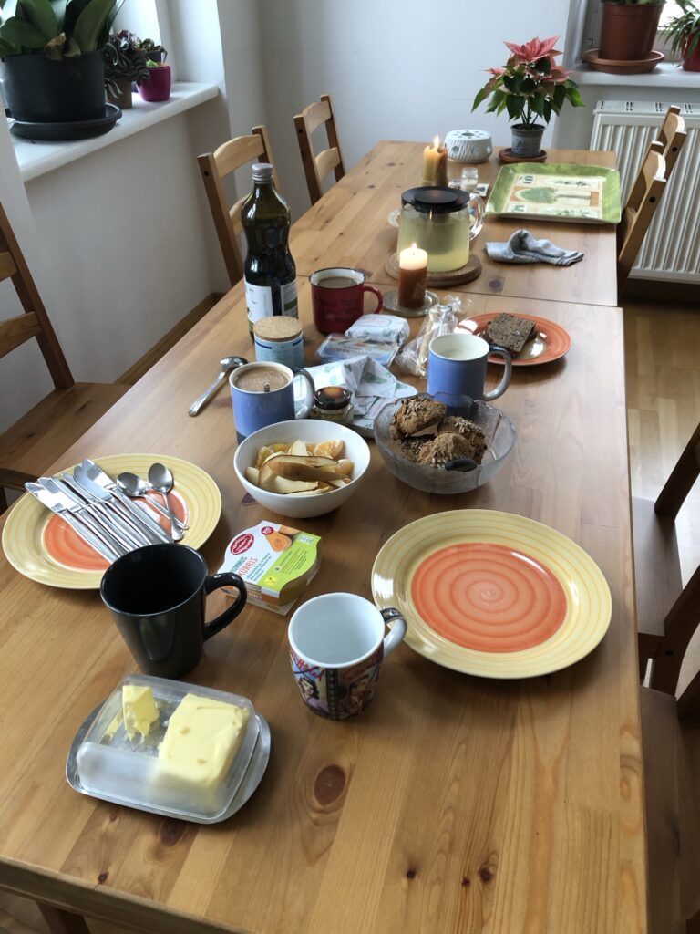 Ein großer Tisch mit Tee, verschiedenen Tassen mit Getränken, Brötchen, Aufstriche, Butter, zwei Teller, im Hintergrund ein Weihnachtsstern. 