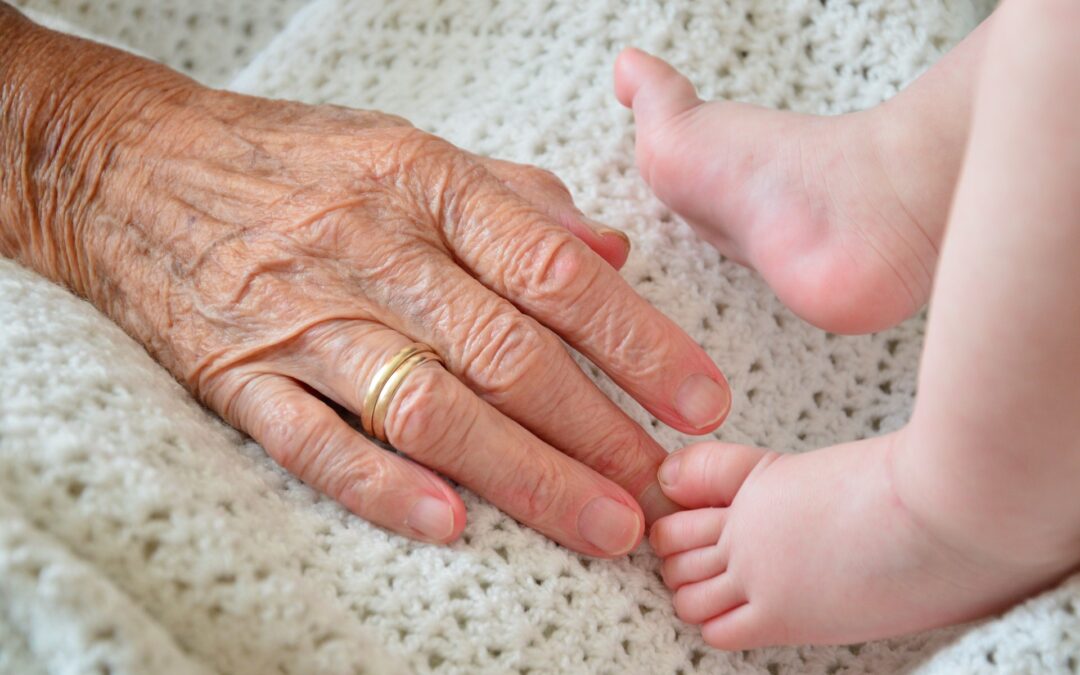 Hand einer alten Frau und die Füße eine Kleinkinds nebeneinander als Symbol der transgenerationalen Verbindung