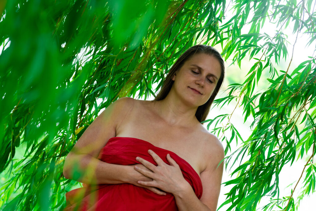 Eine Frau umgeben von grünen Blättern, die in ein rotes Tuch eingewickelt mit geschlossenen Augen die Hände auf der Brust übereinander gelegt hat. 
Ein Sinnbild für die Verbindung zu sich selbst, dem eigenen Körper, den eigenen Bedürfnissen. 