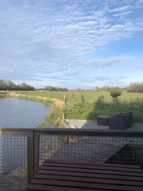 Ausblick aus dem Fenster auf einen Fluss, Felder und eine Terrasse in einem unserer Quartiere in den Niederlanden.