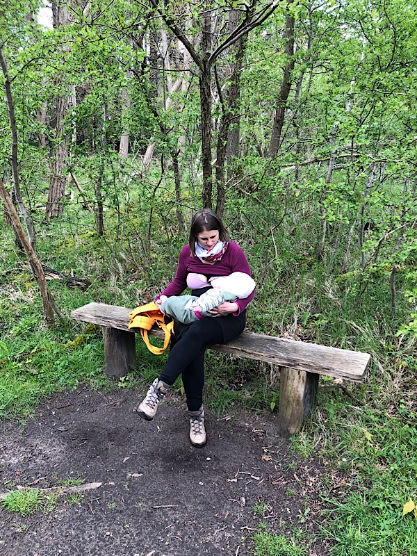 Ich mit dem Baby an der Brust in der Natur auf einer Bank im Wald.