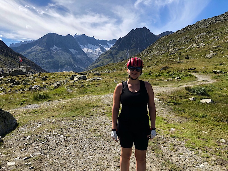 Ich stehe mit Fahrradkleidung und Helm vor einer Bergkulisse. 