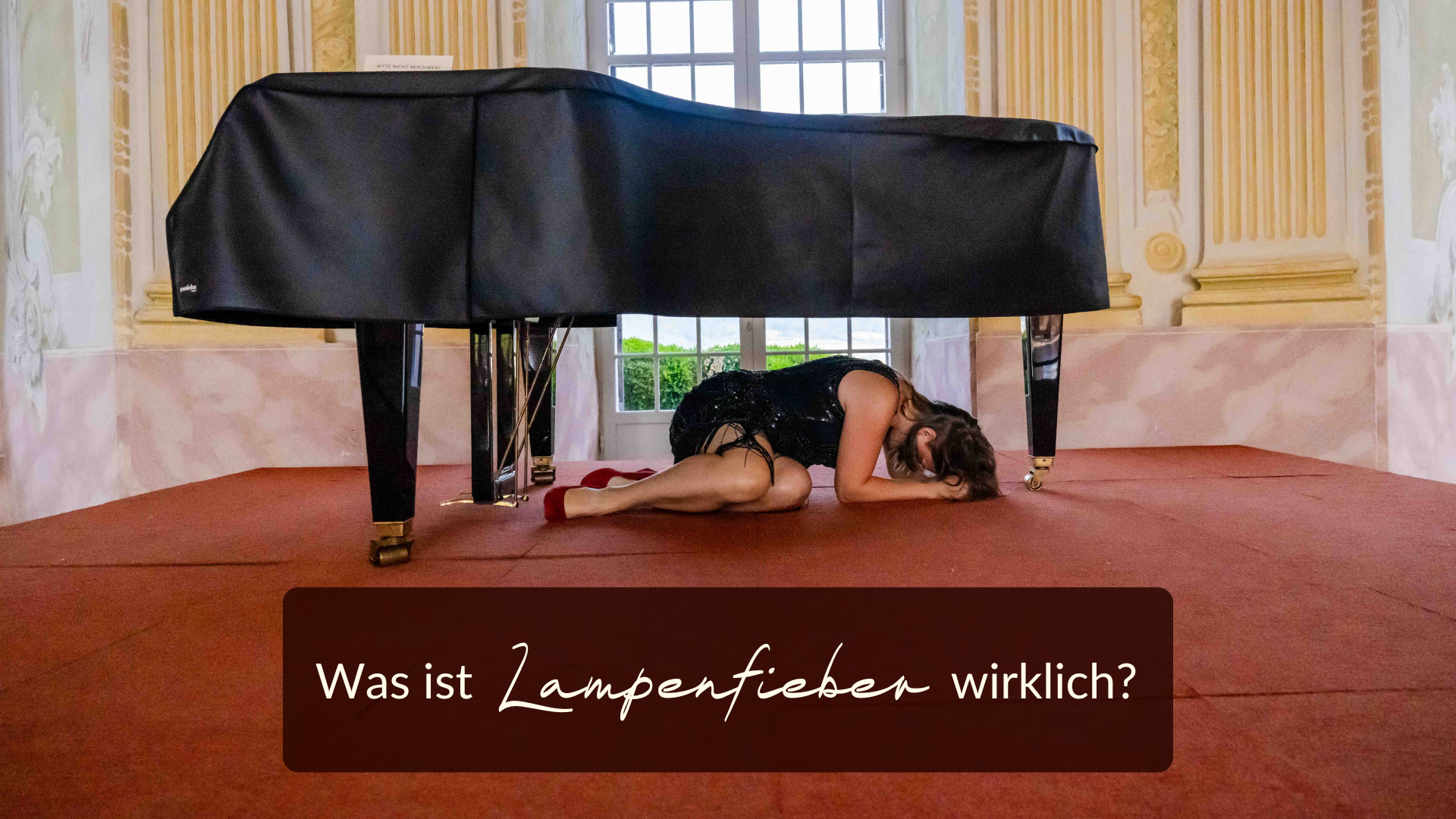 Was ist Lampenfieber? Eine Person in einem schwarzen Kleid liegt auf einem roten Teppich unter einem Flügel in einem reich verzierten Raum und denkt über die Frage nach: „Was ist Lampenfieber wirklich?“.