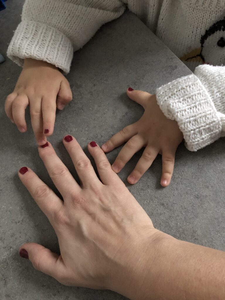 Generoses Hand mit rotem Glitzer-Nagellack und daneben zwei Kinder-Hände mit jeweils einem lackierten Fingernagel.