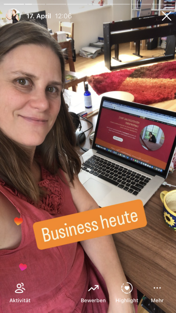 Generose sitzt in einem roten Kleid und offenen Haaren an ihrem Schreibtisch. Im Hintergrund zu sehen das Zimmer mit einem E-Piano, einem rot-orange-gelben Teppich und auf dem Schreibtisch ihr Laptop.