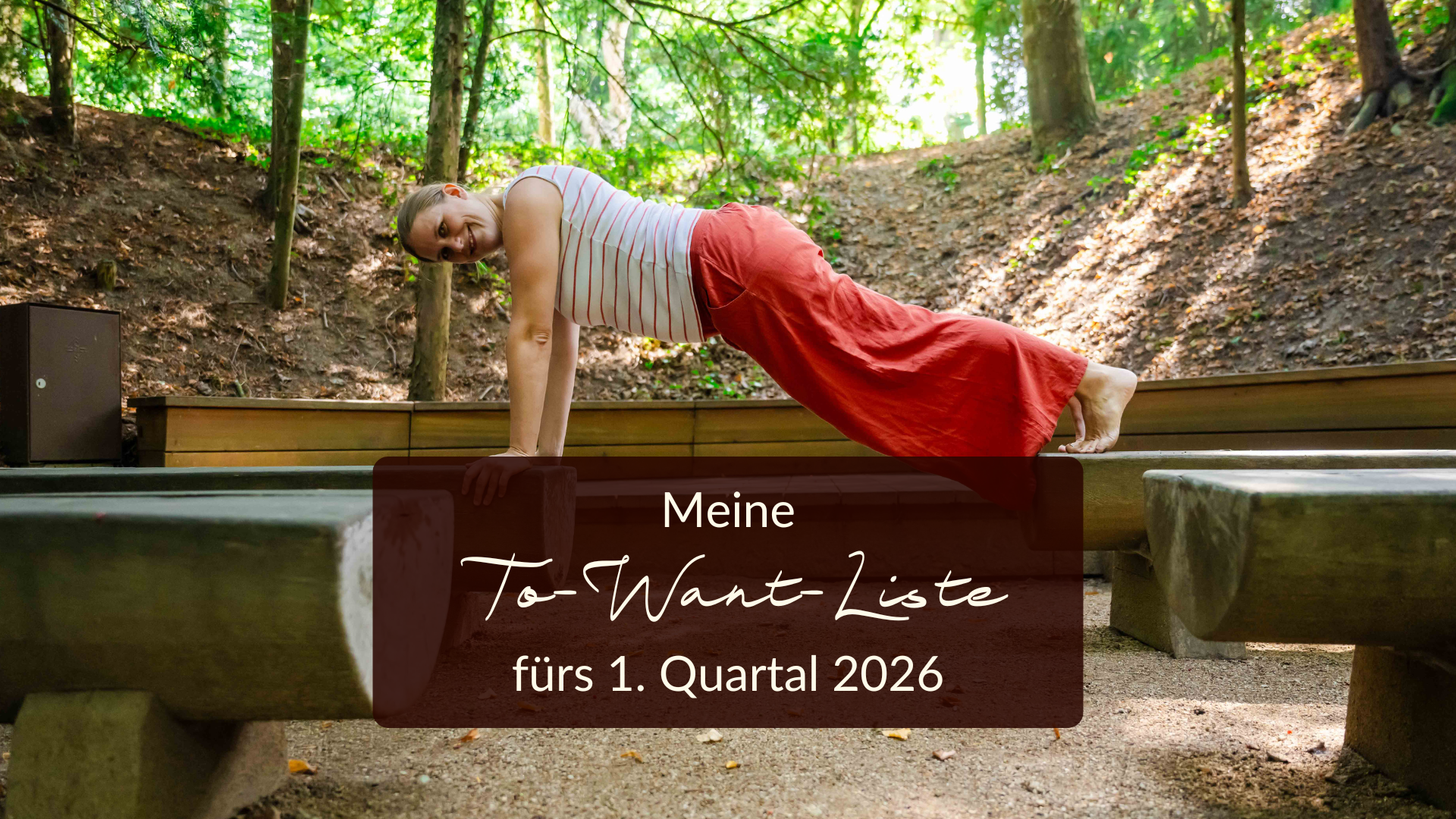 Generose stützt sich mit Füßen und Händen in Plank-Stellung auf zwei Holzbänke, die im Wald stehen und schaut seitlich in die Kamera. Sie trägt eine orange Hose und ein weiß-orange gestreiftes Shirt.