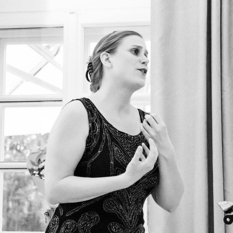 Unstuck Your Voice Generose in einem schwarzen Glitzerkleid singt gerade sehr gefühlvoll. Sie hat beide Hände vor der Brust zu einer Geste geformt und gibt sich dem Ausdruck hin. Das Bild ist in schwarz-weiß.