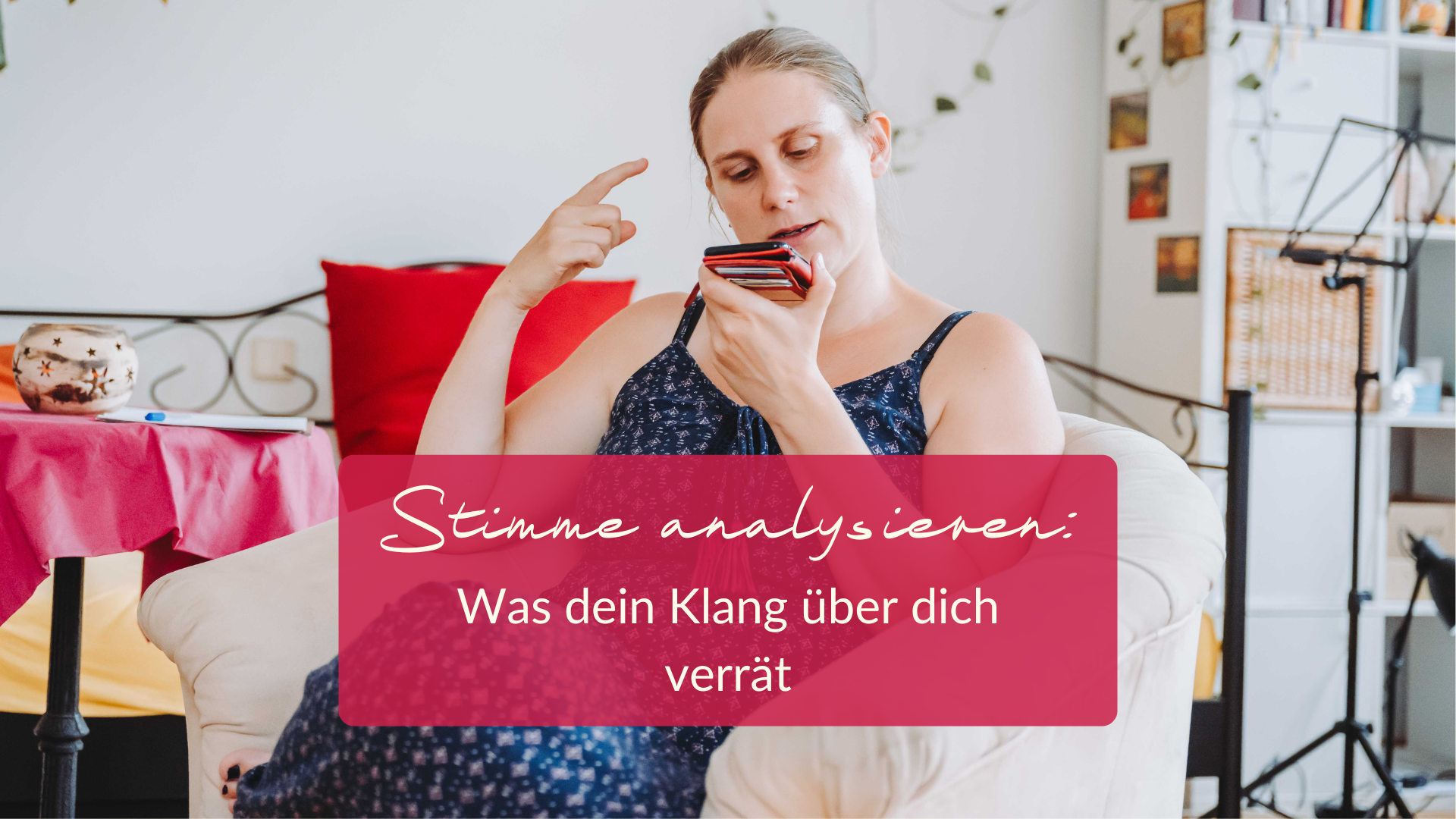 Stimme analysieren Generose sitzt in einem blauen Sommerkleid im Sessel und spricht in ihr Handy. Sie gestikuliert. Im Hintergrund ist ein Tisch mit einer pinken Tischdecke, ein Sofa und ein Notenständer zu sehen. Auf dem Bild ist ein Kasten in dem steht: "Stimme analysieren: Was dein Klang über dich verrät"
