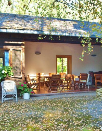 Außenaufnahme eines Hauses mit gemütlichen Bänken davor, Bäumen und Grünfläche.