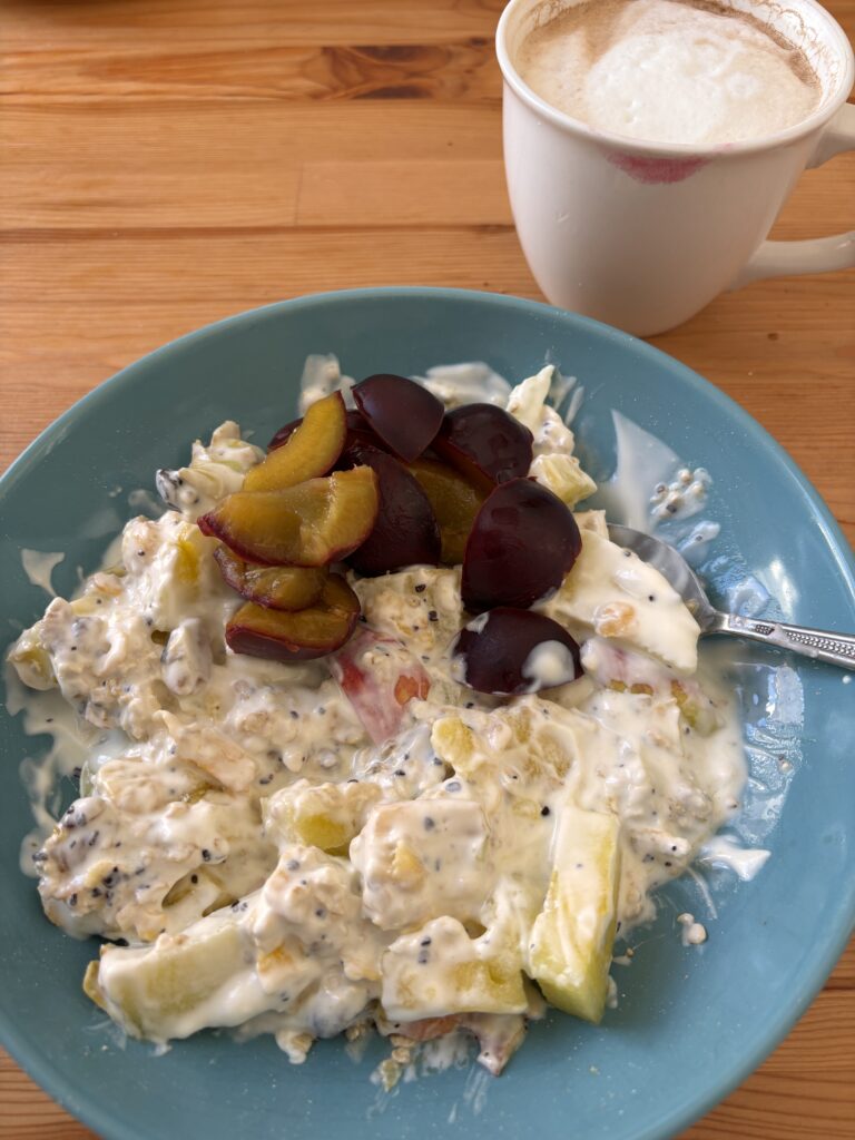 Ein Teller mit Müsli, Joghurt und Früchten, daneben eine Tasse Kaffee mit aufgeschäumter Milch.