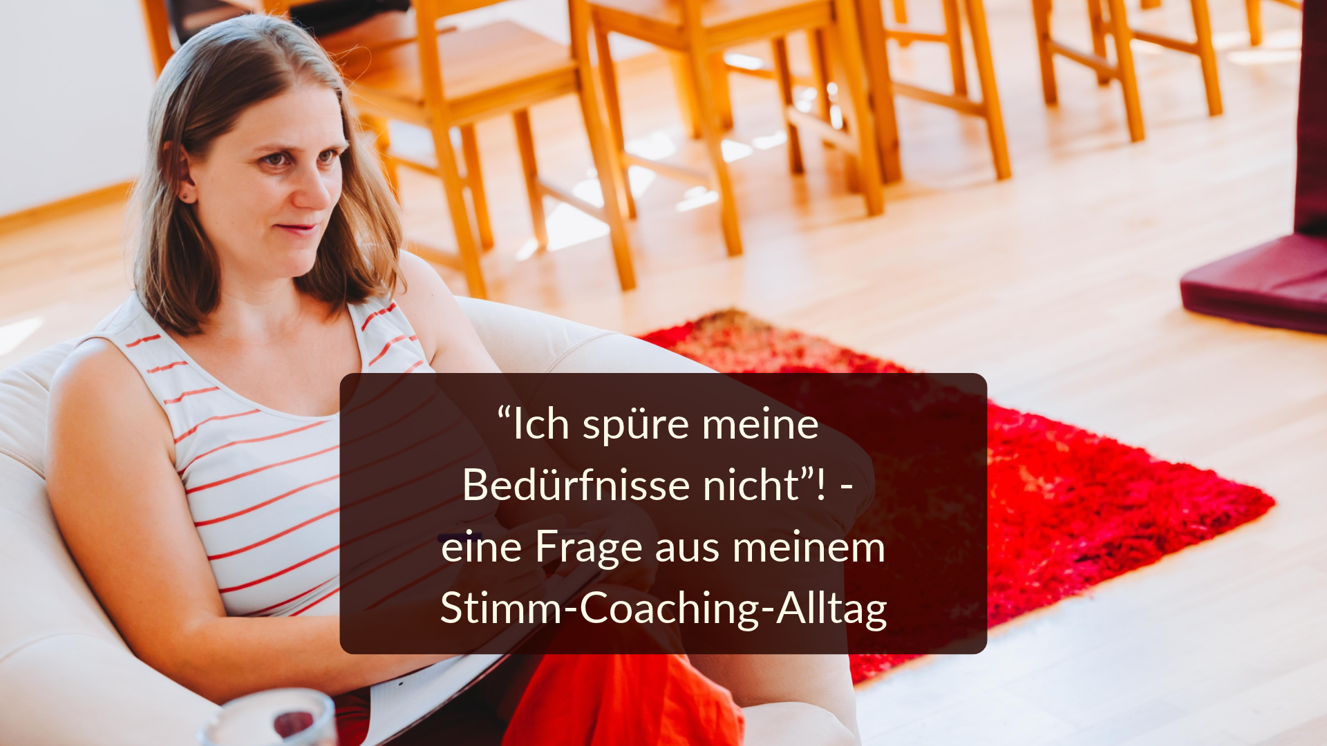 Beduerfnisse Generose sitzt mit einem Block und einem Stift auf ihrem Sessel und hört jemandem zu (diese Person sieht man nicht). Im Hiintergrund sind ein rot, orange, gelber Teppich und Stuhl- und Tischbeine zu sehen. Auf dem Bild die Aufschrift: "Ich spüre meine Bedürfnisse nicht!" - eine Frage aus meinem Stimm-Coaching-Alltag